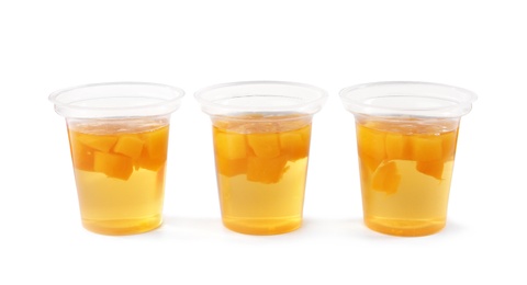 Photo of Tasty jelly desserts with slices of fruit in plastic cups on white background