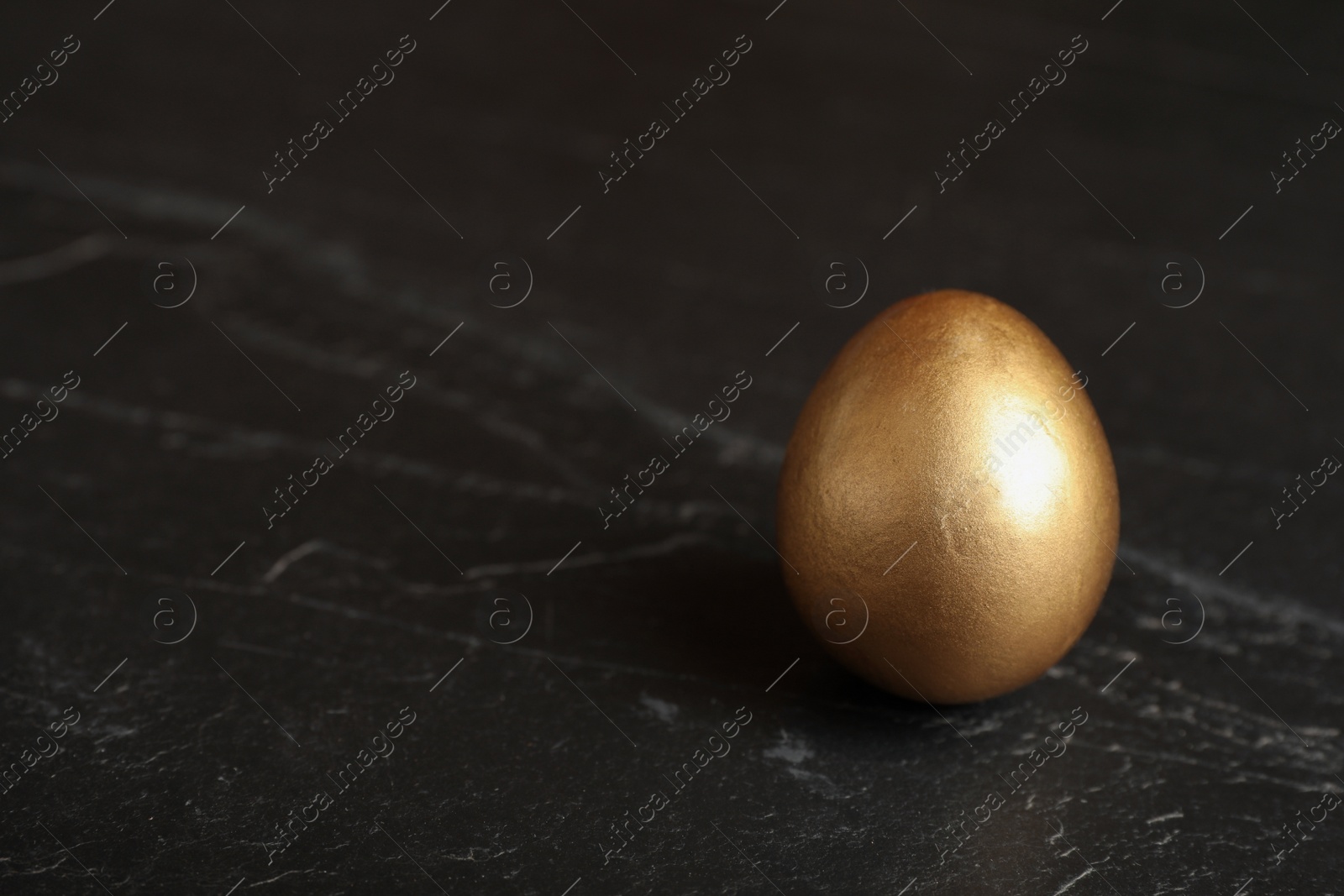 Photo of Shiny golden egg on black table, closeup. Space for text