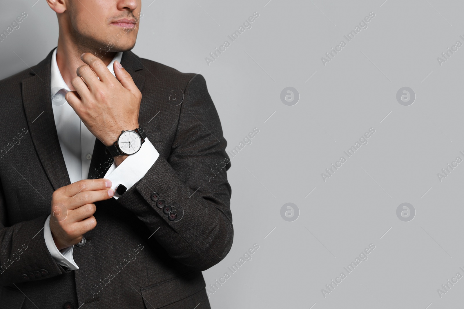 Photo of Stylish man putting on cufflink against grey background, closeup. Space for text