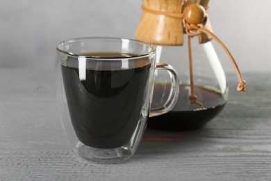 Photo of Glass and chemex coffeemaker with tasty drip coffee on grey wooden table, closeup
