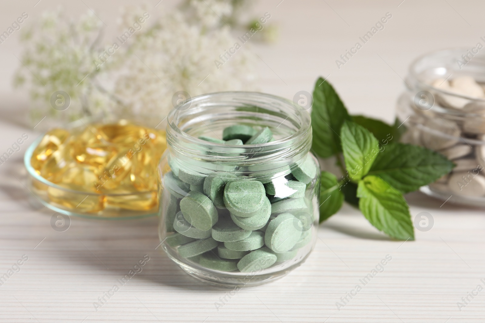 Photo of Jars with different pills and mint on white wooden table, closeup. Dietary supplements