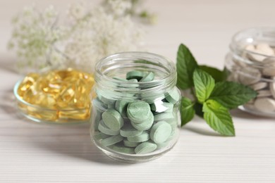 Photo of Jars with different pills and mint on white wooden table, closeup. Dietary supplements