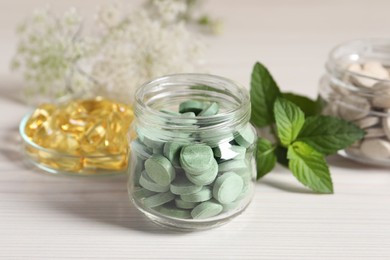 Jars with different pills and mint on white wooden table, closeup. Dietary supplements