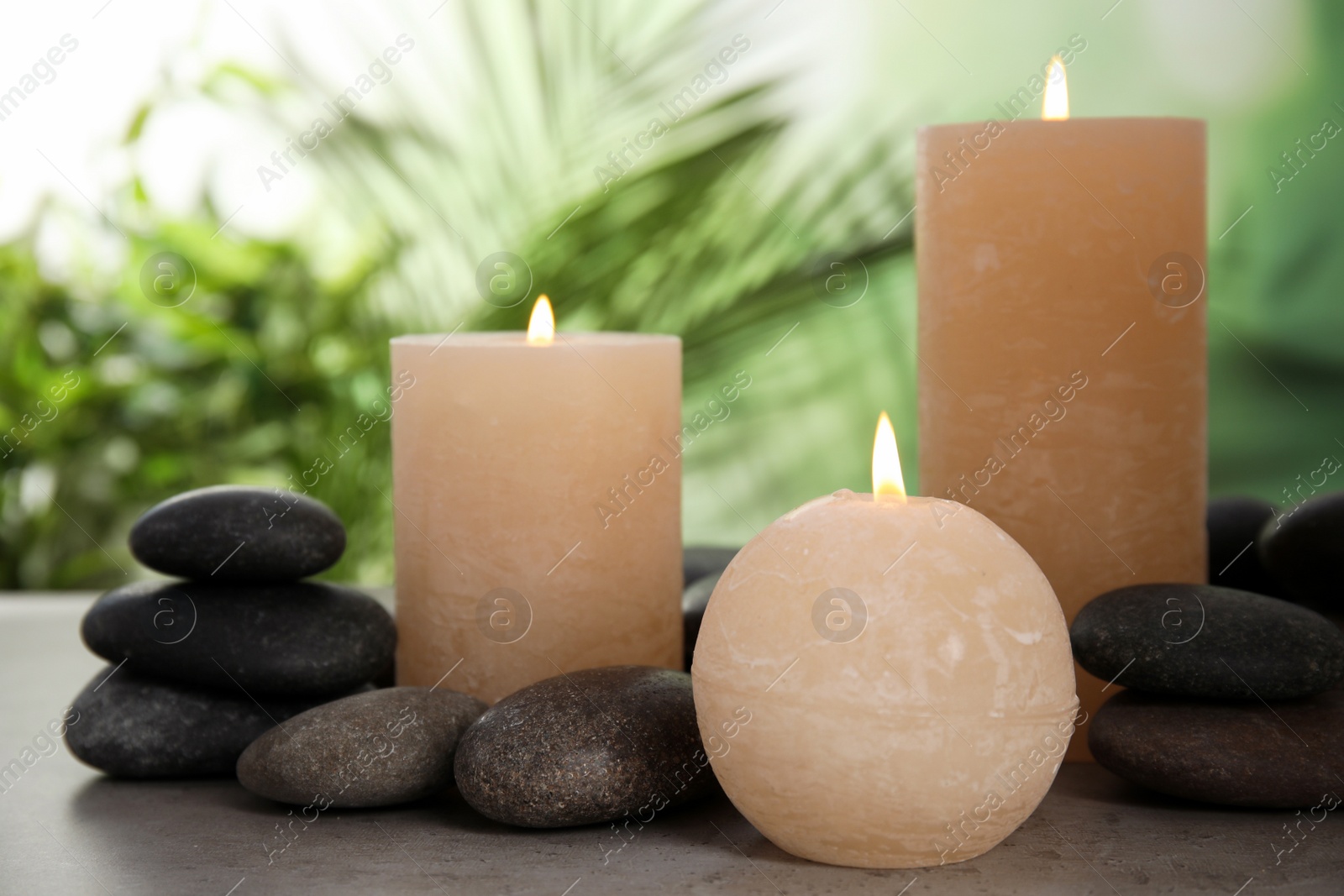 Photo of Burning candles and spa stones on table against blurred green background