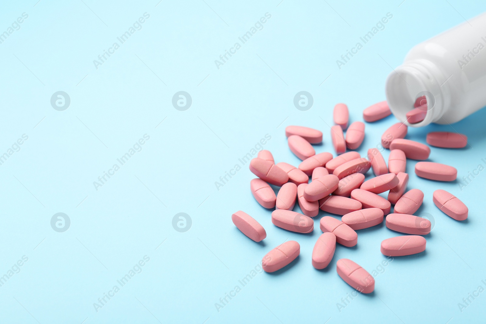 Photo of Vitamin pills and bottle on light blue background, closeup. Space for text