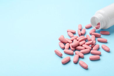 Photo of Vitamin pills and bottle on light blue background, closeup. Space for text