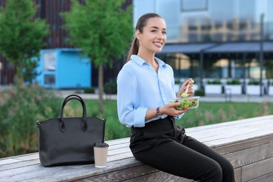 Photo of Smiling businesswoman eating lunch during break outdoors
