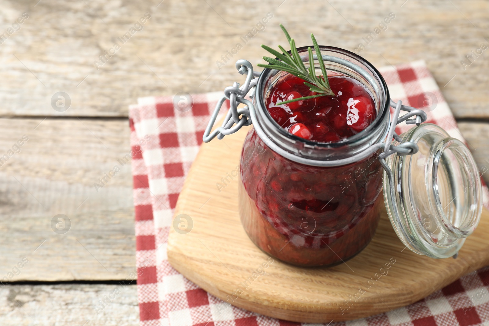 Photo of Fresh cranberry sauce in glass jar and rosemary on light wooden table, space for text