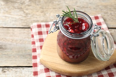 Photo of Fresh cranberry sauce in glass jar and rosemary on light wooden table, space for text