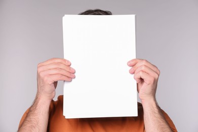 Man covering face with sheet of paper on light grey background. Mockup for design