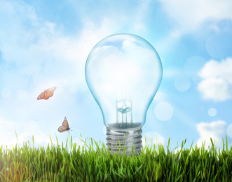 Image of Solar energy concept. Glowing light bulb in green grass and blue sky with clouds on background