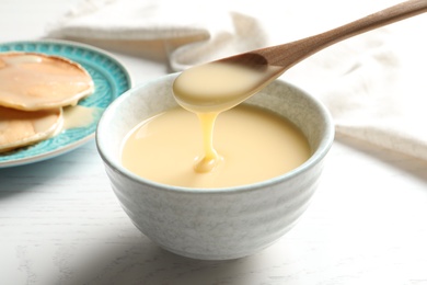 Spoon of pouring condensed milk over bowl on table, closeup. Dairy products