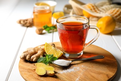 Photo of Cup of delicious ginger tea and ingredients on white wooden table