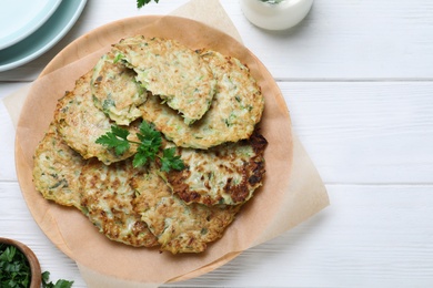 Delicious zucchini fritters served on white wooden table, flat lay