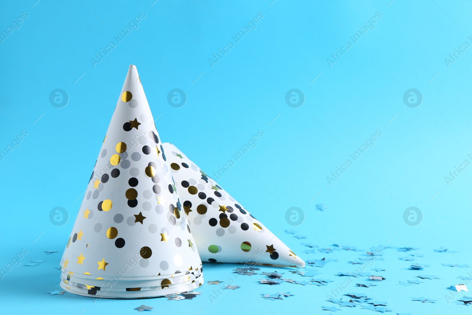 Photo of Party hats and confetti on light blue background, space for text