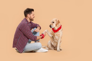 Cute Labrador Retriever giving paw to man on beige background