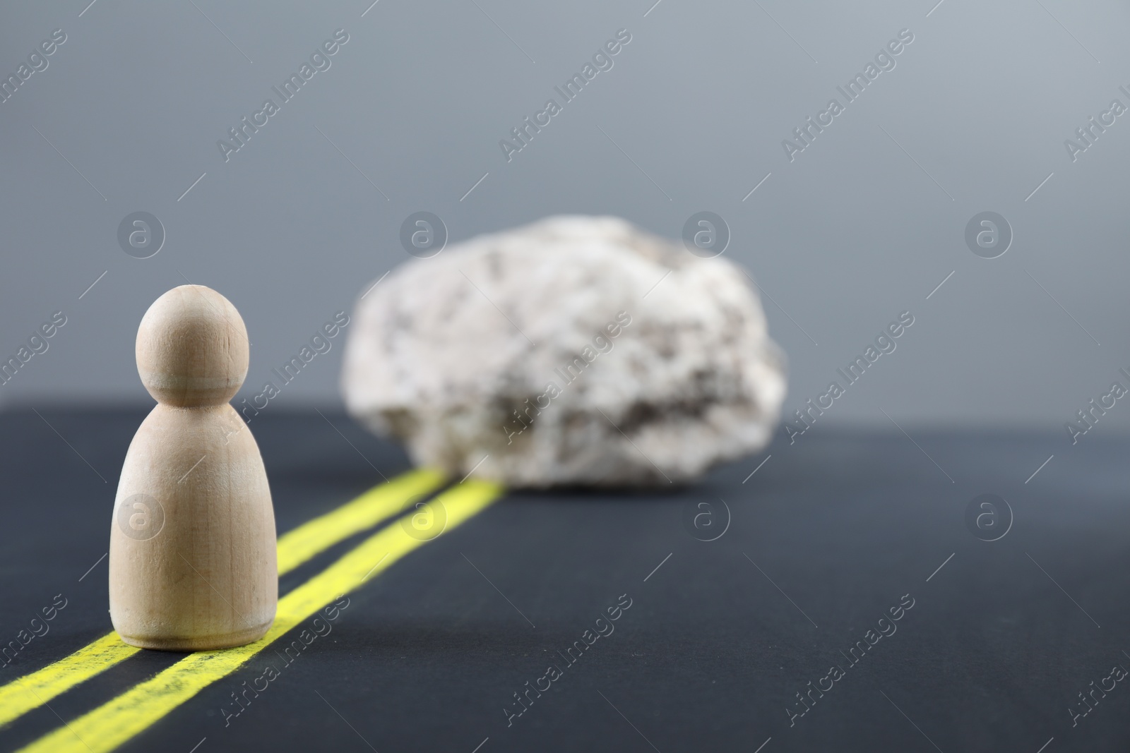 Photo of Overcoming barries for development and success. Wooden human figure movement blocked by stone on road, space for text