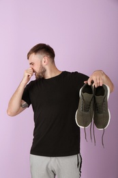 Photo of Young man feeling bad smell from shoes on color background. Air freshener