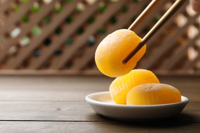 Taking delicious mochi from plate with chopsticks on wooden table, space for text. Traditional Japanese dessert