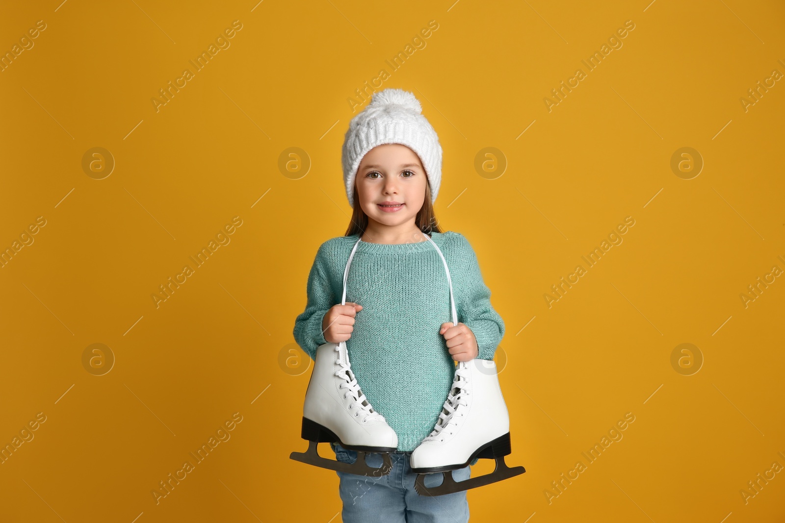 Photo of Cute little girl in turquoise knitted sweater with skates on yellow background