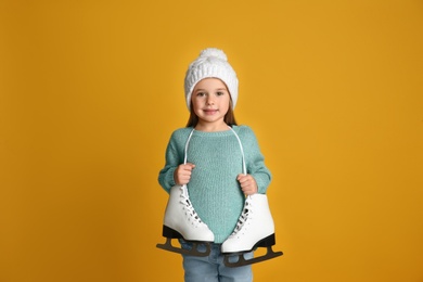 Photo of Cute little girl in turquoise knitted sweater with skates on yellow background
