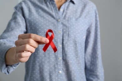 Photo of Woman holding red awareness ribbon on grey background, closeup with space for text. World AIDS disease day