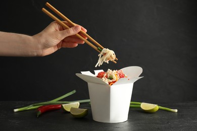 Woman eating vegetarian wok noodles with chopsticks from box at black table, closeup