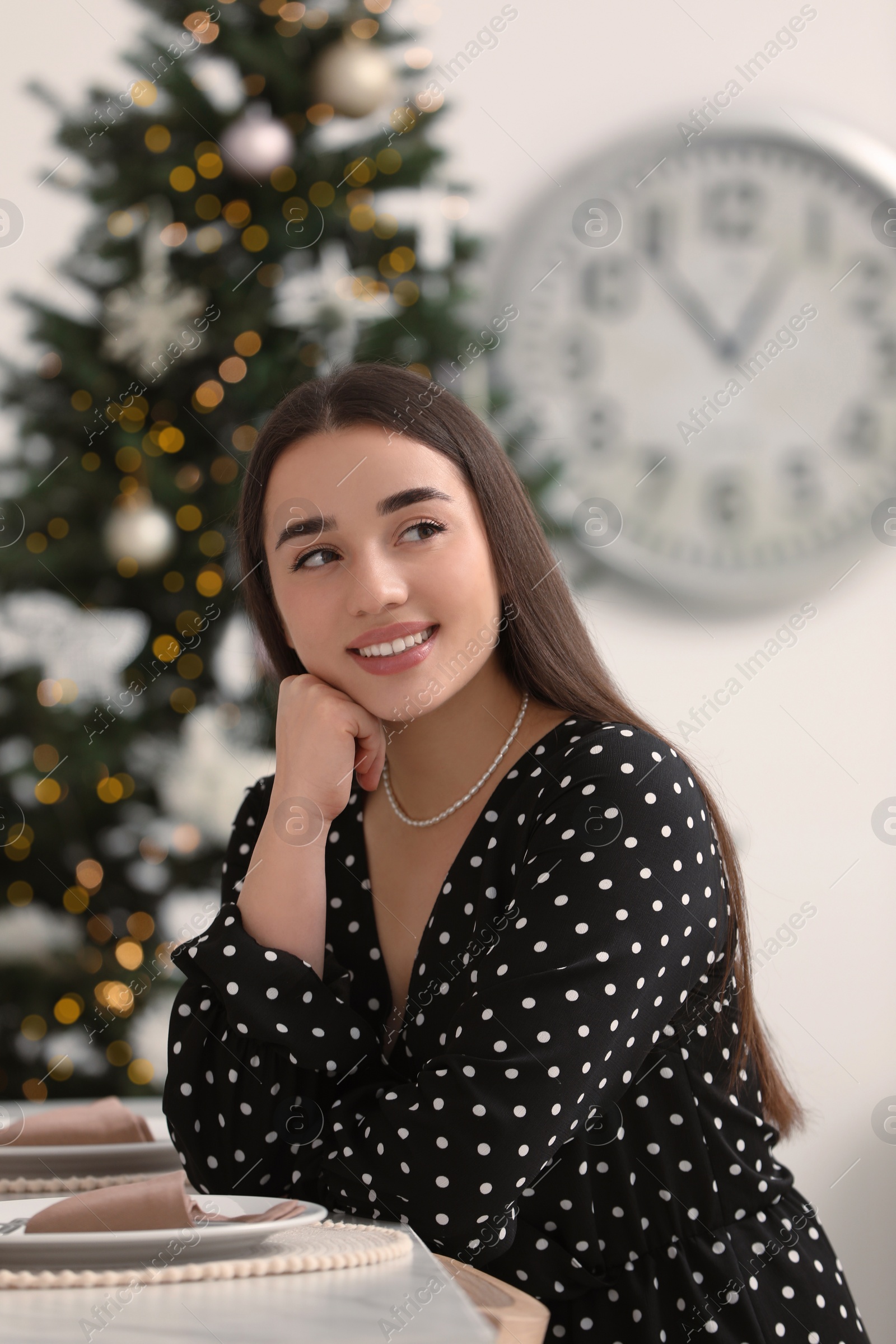 Photo of Happy woman sitting at table near Christmas tree indoors