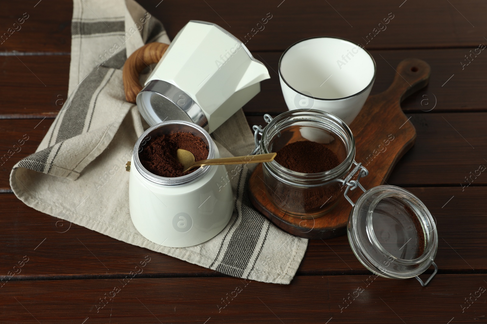 Photo of Moka pot, cup, ground coffee and kitchen towel on wooden table