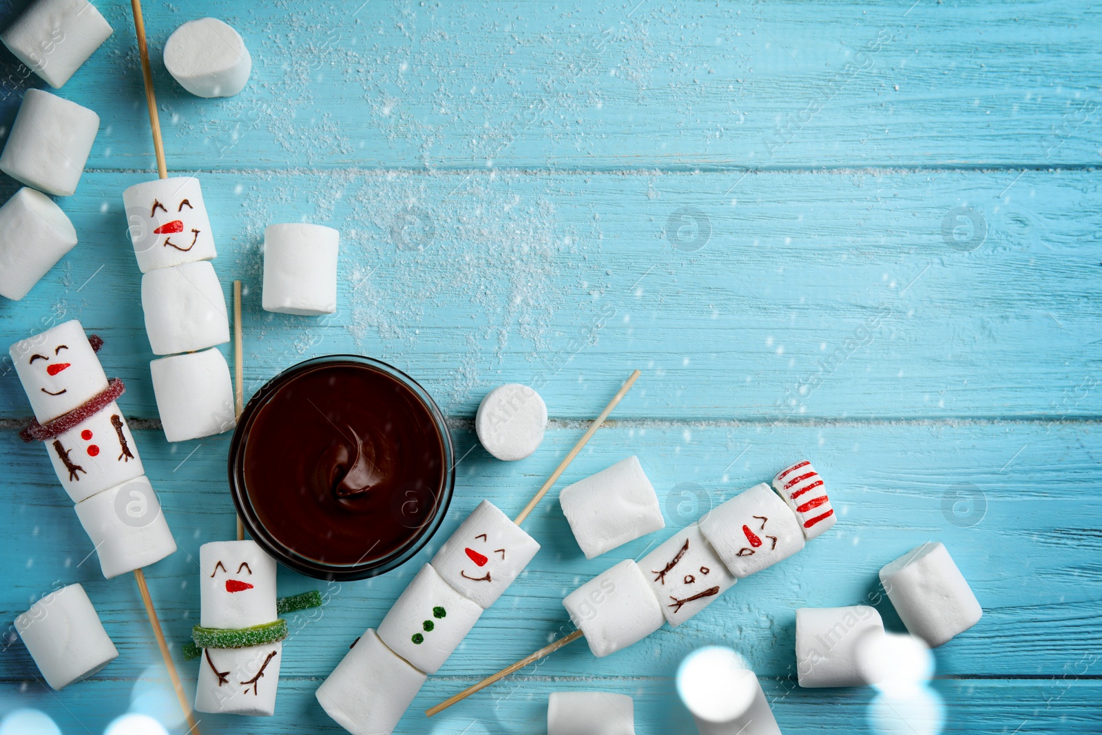 Image of Snowmen made of marshmallows and chocolate paste on light blue wooden background, flat lay. Space for text