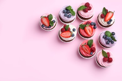 Different delicious cupcakes with cream and berries on pink background, flat lay. Space for text