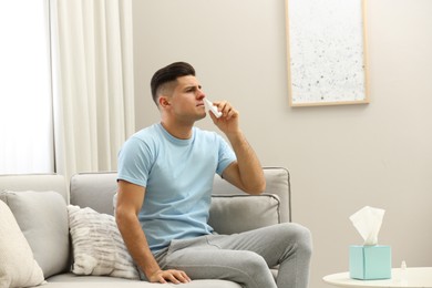 Photo of Ill man using nasal spray on sofa at home
