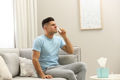 Ill man using nasal spray on sofa at home