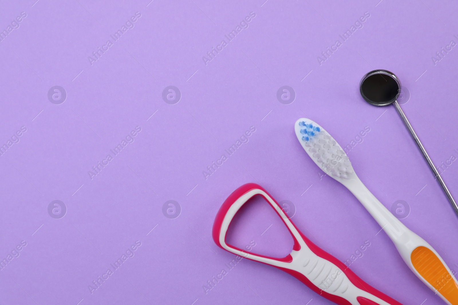 Photo of Tongue cleaner, toothbrush and dentist mirror on violet background, flat lay. Space for text