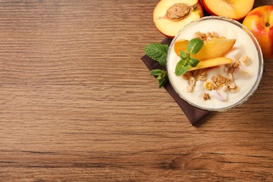 Photo of Tasty peach yogurt with granola, mint and pieces of fruit in dessert bowl on wooden table, flat lay. Space for text
