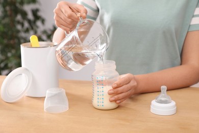 Photo of Woman preparing infant formula at table indoors, closeup. Baby milk