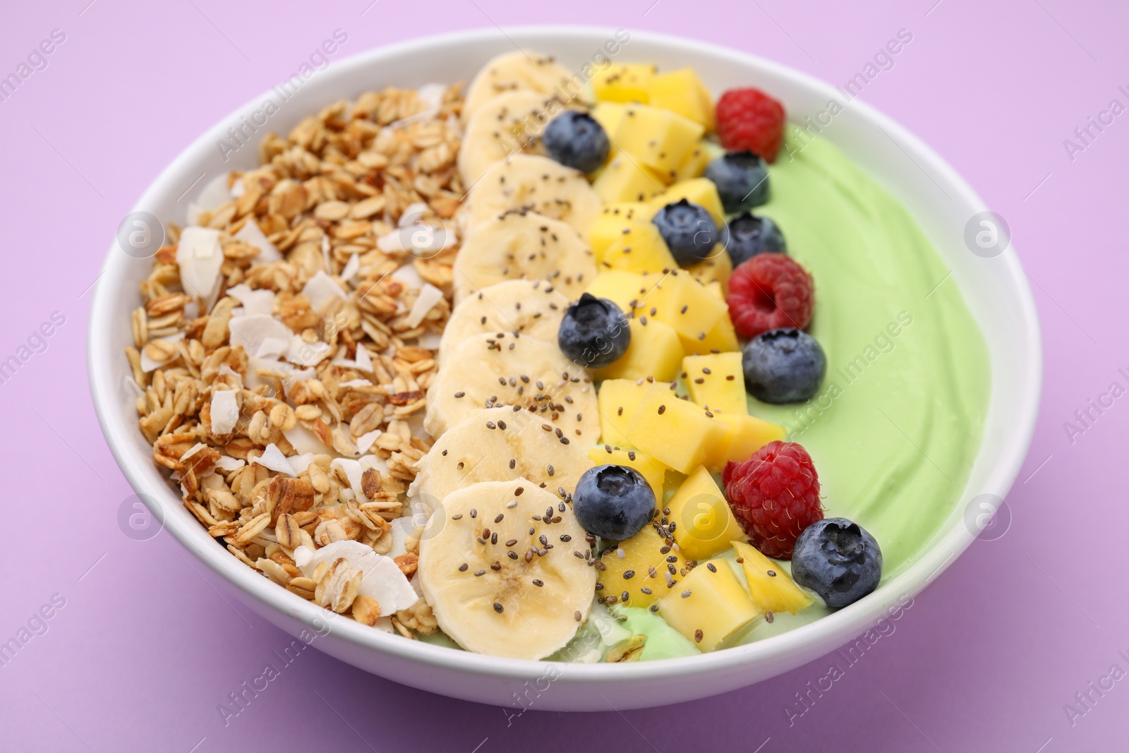 Photo of Tasty matcha smoothie bowl served with fresh fruits and oatmeal on violet background, closeup. Healthy breakfast