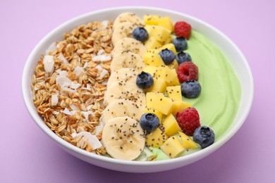 Photo of Tasty matcha smoothie bowl served with fresh fruits and oatmeal on violet background, closeup. Healthy breakfast