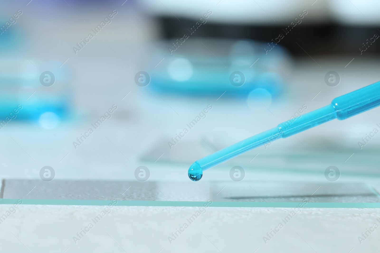 Photo of Dripping sample of light blue liquid onto microscope slide on white table, closeup