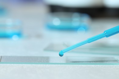 Dripping sample of light blue liquid onto microscope slide on white table, closeup