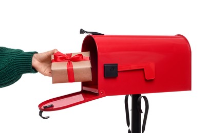 Woman putting Christmas gift into mailbox on white background, closeup. Sending present by mail