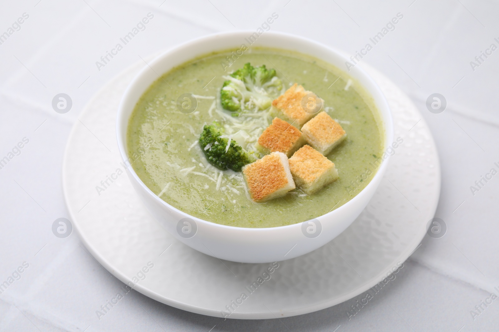 Photo of Delicious broccoli cream soup with croutons and cheese on white tiled table, closeup