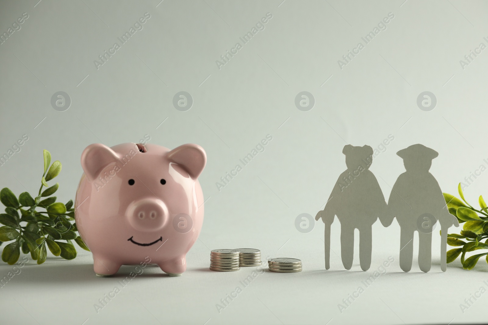 Photo of Pension savings. Figure of senior couple, piggy bank, coins and green twigs on grey background