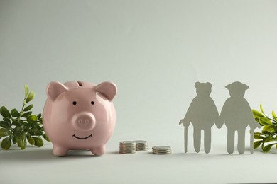 Pension savings. Figure of senior couple, piggy bank, coins and green twigs on grey background