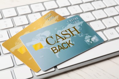 Cashback credit cards and keyboard on white wooden table, closeup