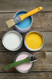 Cans of colorful paints with brushes on wooden table, flat lay