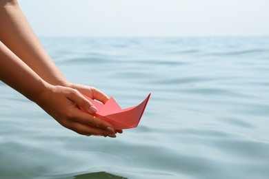 Woman holding pink paper boat near sea, closeup. Space for text