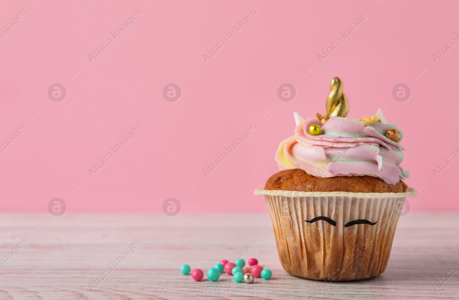 Photo of Cute sweet unicorn cupcake on white wooden table against pink background, space for text