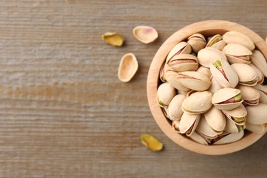 Photo of Tasty pistachios in bowl on wooden table, top view. Space for text