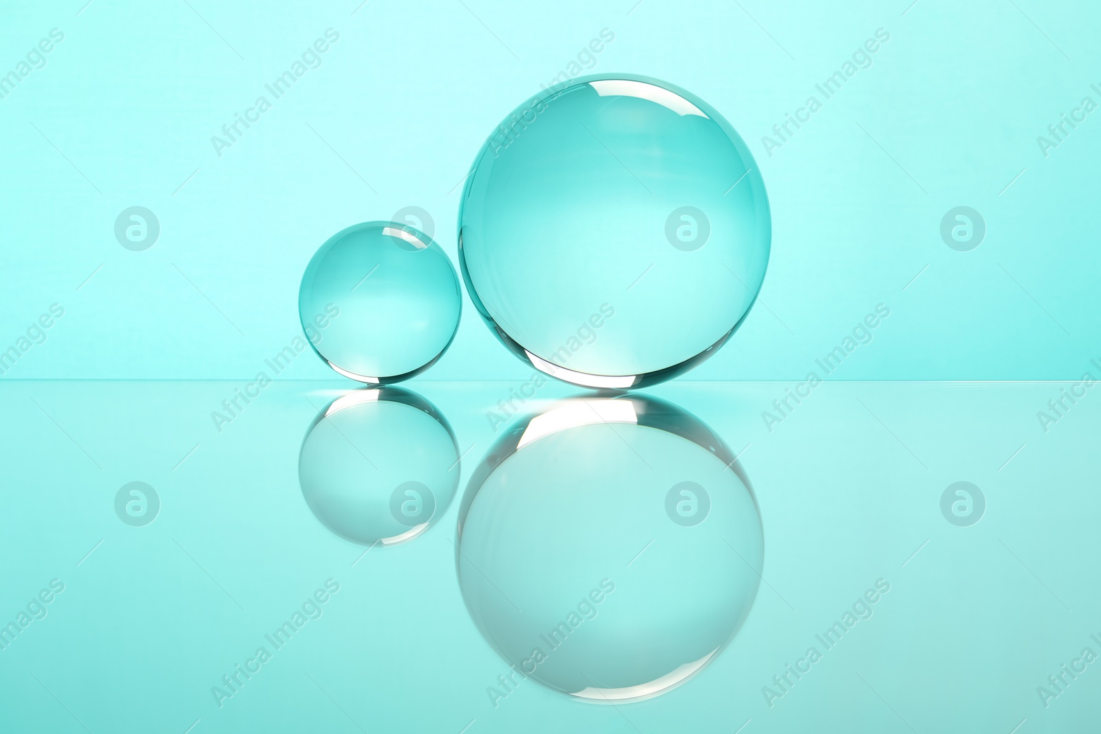 Photo of Transparent glass balls on mirror surface against turquoise background